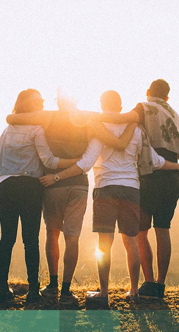 four person hands wrap around shoulders while looking at sunset